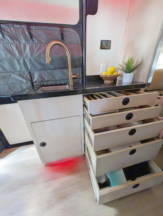 RV rental kitchen with a golden sink, black countertop, and multiple open drawers showing organized storage solutions.. New Life Conversions Luxury Edition 2022