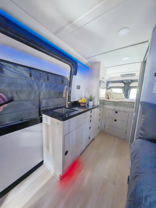 RV rental interior: modern kitchenette with sink, bed, and ambient blue/red lighting. Compact, functional design.. New Life Conversions Luxury Edition 2022