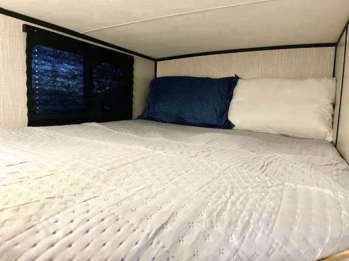 Cozy RV rental interior: A comfortable bunk bed with white bedding, blue and white pillows, and a window blind.. Heartland M-3385 2021