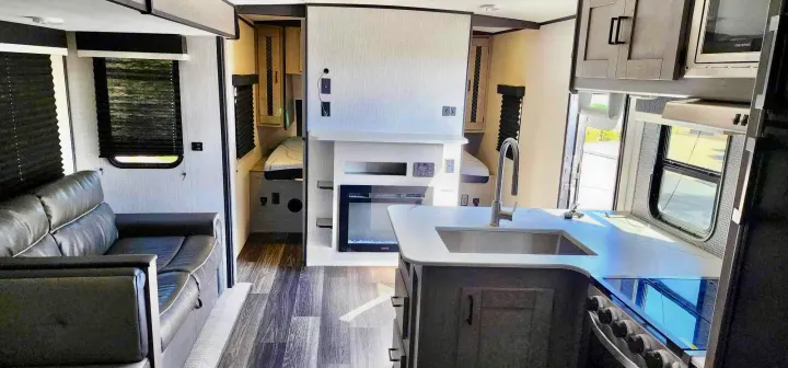 Modern RV rental interior with kitchen, living area sofa, and versatile bunk/fireplace unit.. Heartland M-3385 2021