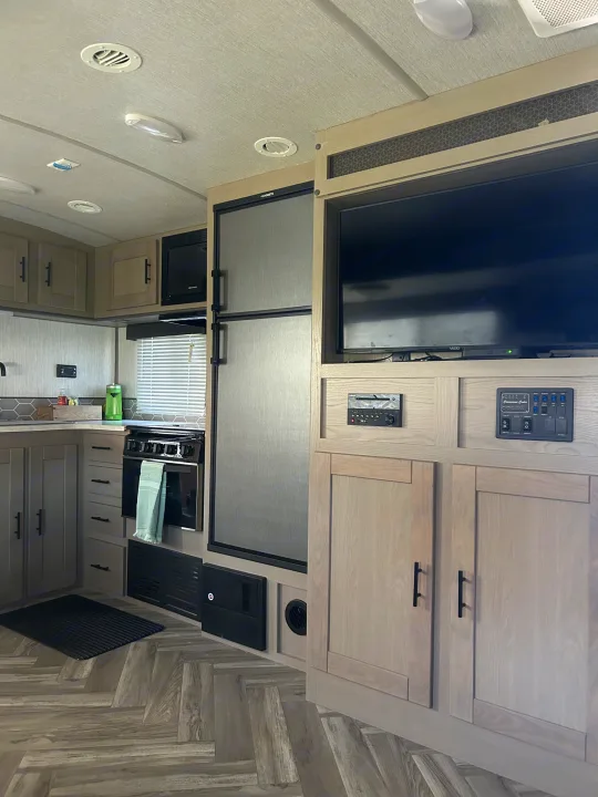Inside a well-equipped RV rental: kitchen with stove/microwave, Dometic fridge, TV, and control panel.. Shadow Trailers Shadow Cruiser 2020