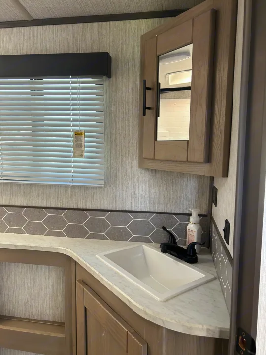 RV rental bathroom features a light-toned vanity with a white sink, black faucet, and mirrored cabinet above a tiled backsplash.. Shadow Trailers Shadow Cruiser 2020