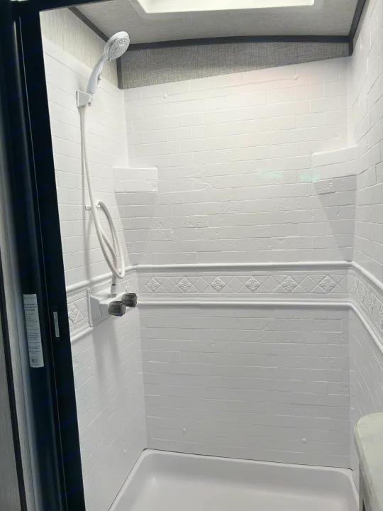 Spotless RV shower interior, featuring white brick-textured walls, decorative trim, and a handheld shower, perfect for RV rental.. Shadow Trailers Shadow Cruiser 2020