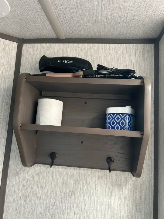 RV rental bathroom storage: A wall shelf organizes toiletries, a hairdryer, and toilet paper, with hooks below.. Shadow Trailers Shadow Cruiser 2020