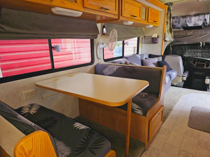 Explore this compact RV rental interior featuring a comfy dinette, overhead cabinets, and sleeping bunks for travel.. Itasca Spirit 2003