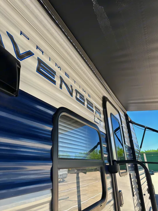 RV rental: Side view of a blue and white Prime Time Avenger LT travel trailer, featuring an extended awning and LED lighting.. Prime Time Avenger - 17BHS 2022