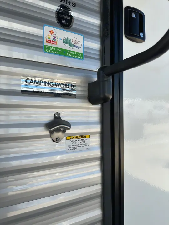 RV side detail: 'Care Camps' & 'Camping World' stickers, a caution notice, and a bottle opener. Ideal for an RV rental adventure.. Prime Time Avenger - 17BHS 2022