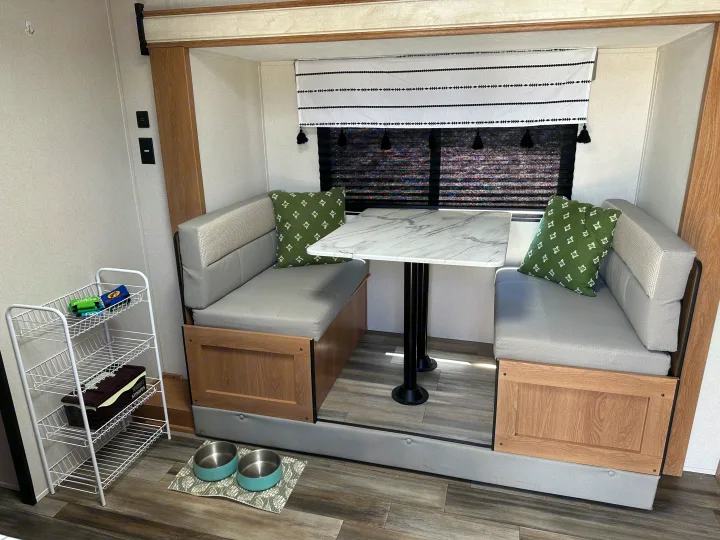 RV rental interior featuring a cozy dinette with light gray benches, a white marble-look table, and pet bowls on the floor.. Prime Time Avenger - 17BHS 2022