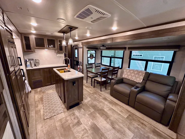 Modern RV rental interior showing kitchen, dining table, and recliner seating. Light wood floors create a bright, inviting space.. Forest River Flagstaff Classic 2022