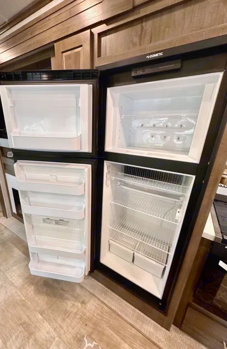 Open Dometic refrigerator and freezer in an RV rental, showcasing empty shelves and door bins for travel convenience.. Forest River Flagstaff Classic 2022