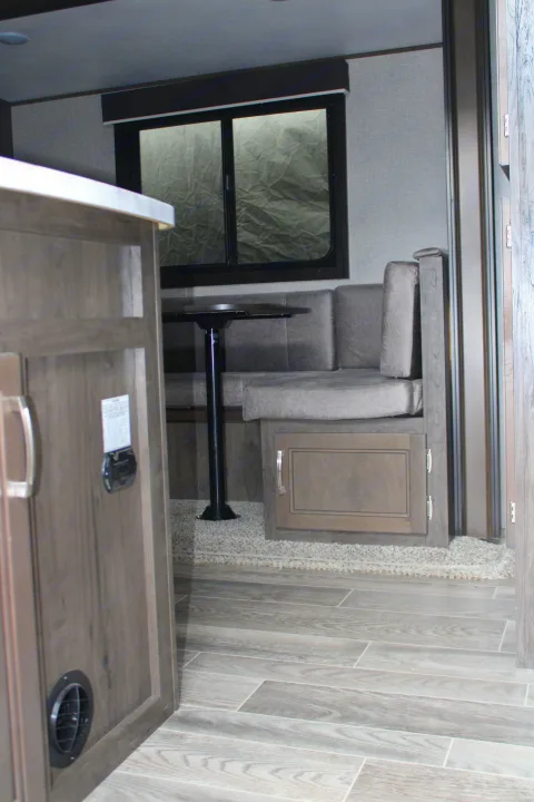 RV rental interior: A modern dinette with gray booth seating, dark table, window, and wood-look flooring. A cabinet is in the foreground.. Jayco Jayflight SLX 8 2021