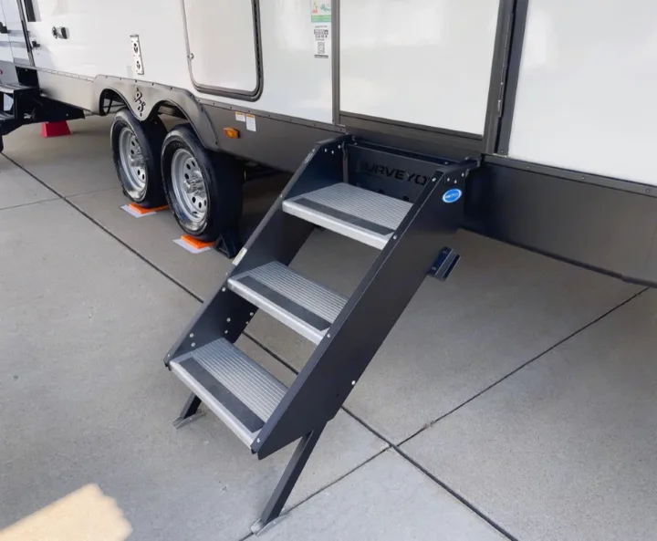 RV rental: White travel trailer with three black entry steps deployed. Wheels rest on orange leveling blocks on concrete.. coachman spirit 2022
