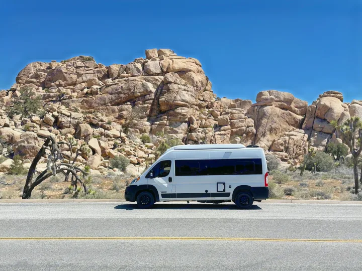 White RV rental on a desert road, framed by huge rock formations and Joshua trees.. Winnebago Solis 2023