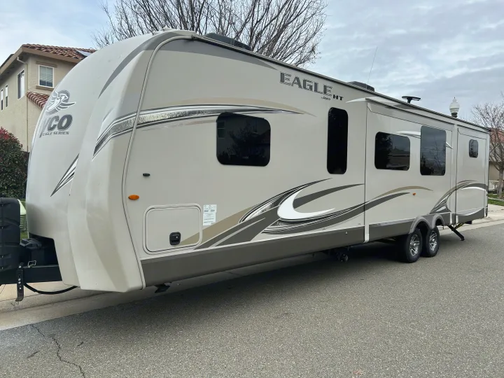 A large, light-colored Jayco Eagle HT travel trailer, often used as an RV rental, is parked on a residential street.. Jayco Eagle HT 2018