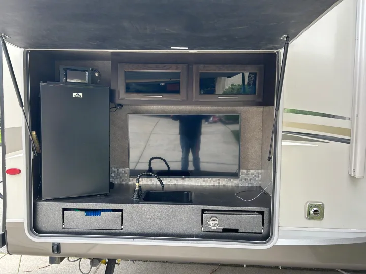 RV rental outdoor kitchen setup featuring a mini-fridge, microwave, TV, sink, and pull-out storage.. Jayco Eagle HT 2018