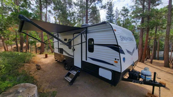 This white travel trailer RV rental, with its awning extended, is perfectly set up for camping in a peaceful forest clearing.. Keystone RV Springdale 2022