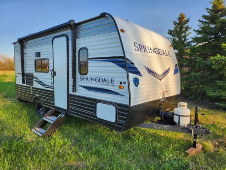Explore nature with this white Springdale travel trailer RV rental, featuring blue accents, extended awning with LED lights, and steps down.. Keystone RV Springdale 2022