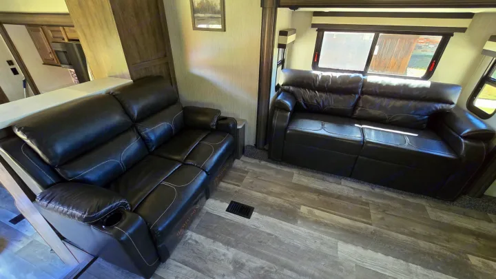 Comfortable RV rental living space featuring two dark leather recliners, wood-look flooring, and bright windows.. Forest River Sandpiper 2021