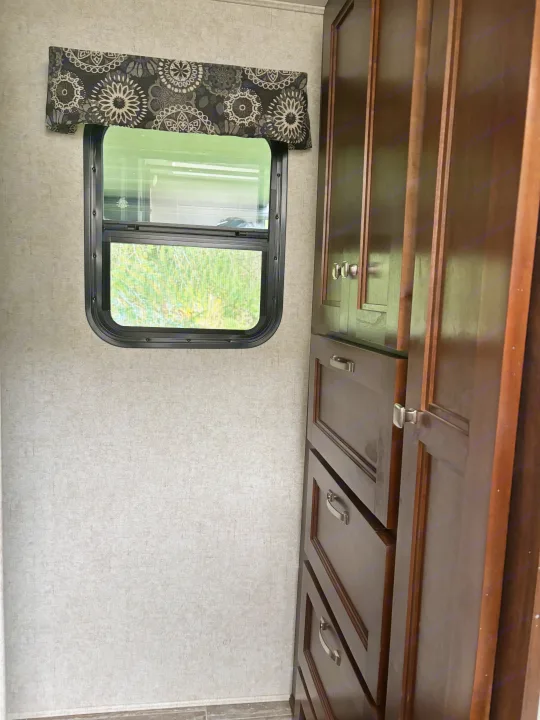 View inside an RV rental: Features a window with a patterned valance and dark wood cabinets with silver hardware.. Forest River Sunseeker 2018