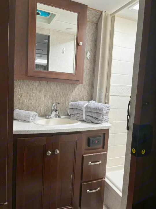 Compact RV rental bathroom features a sink vanity, mirror, and shower, with fresh towels ready for use.. Forest River Sunseeker 2018