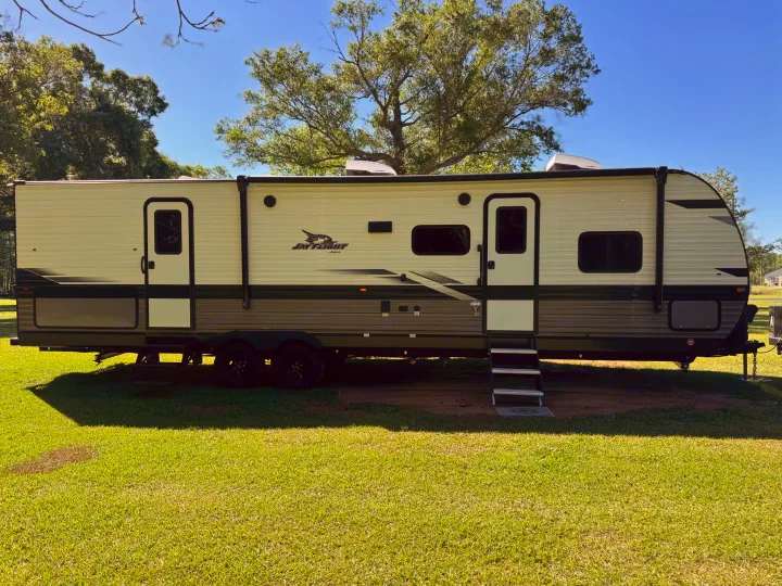 Spacious cream and grey Jay Flight RV rental, with steps down, set on a grassy campsite under a blue sky.. Jayco Jay Flight 324BDS 2024