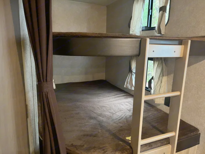 Inside an RV rental: a cozy bunk bed setup with soft bedding, windows, and ladder for travel comfort.. Coachmen Catalina 2020
