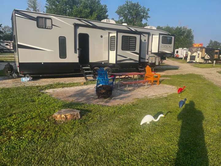 This large gray RV rental, a fifth-wheel toy hauler, is set up at a spacious campsite with a patio, picnic area, and fire pit.. Forest River Cherokee Arctic Wolf 2022