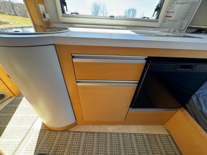 RV rental galley kitchen features: sleek counter, sink, cooktop, fridge, and wooden storage. Window view.. nuCamp T@B 2018