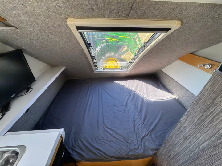 Cozy RV rental interior with a comfy bed, overhead skylight view of a John Deere tractor, plus a TV.. nuCamp T@B 2018