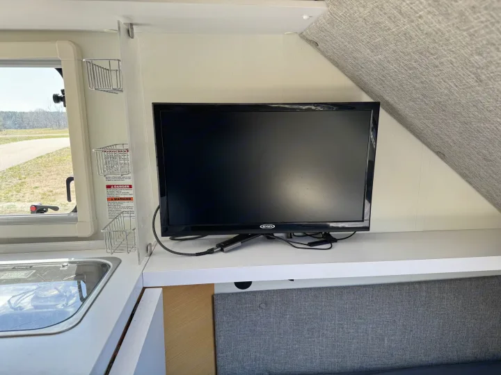 An RV rental's cozy interior features a mounted TV, compact kitchen, and a comfortable gray seating area.. nuCamp T@B 2018