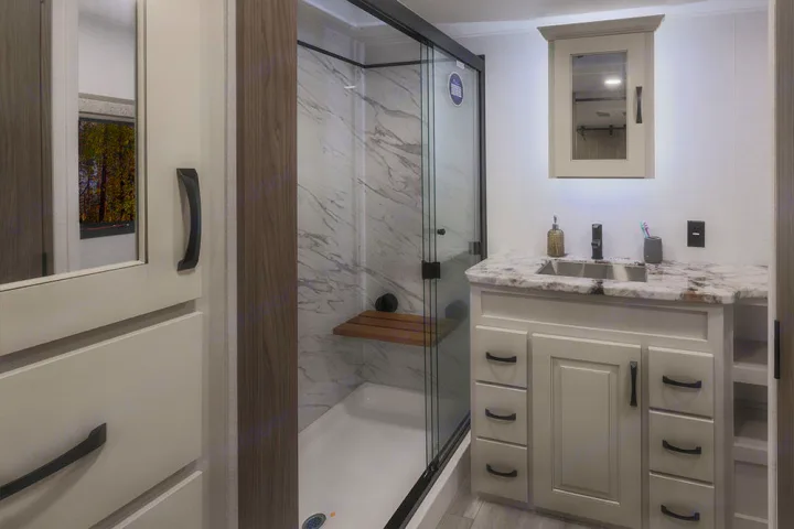 Modern RV rental bathroom with a spacious shower, marble-look vanity, and functional storage, offering comfort on the go.. Alliance RV Paradigm 2021