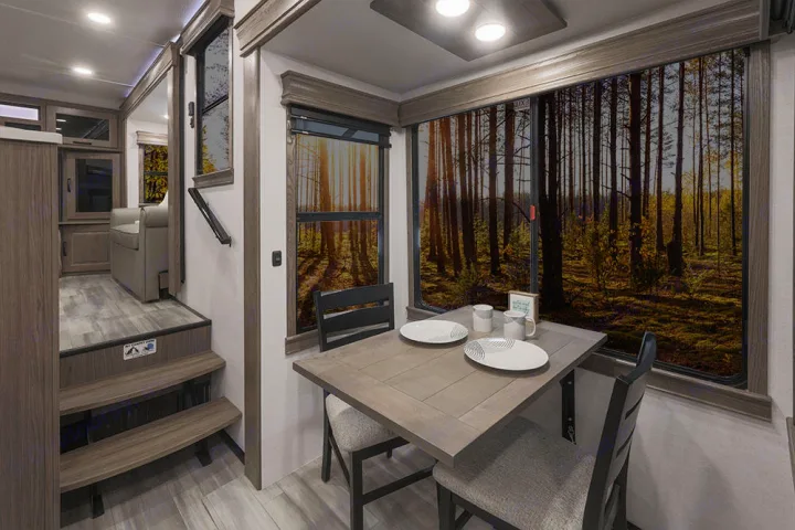 Modern RV rental interior with dining area, forest view through large windows, and steps leading to the living space.. Alliance RV Paradigm 2021