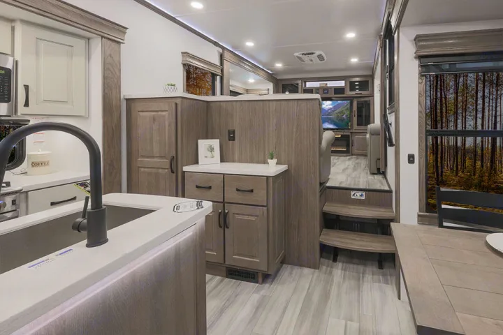 Spacious RV rental interior: modern kitchen with a sink, elevated living area, and large windows with forest views for your trip.. Alliance RV Paradigm 2021