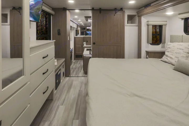 This spacious RV rental bedroom features a comfortable bed, dresser with TV, and a modern sliding barn door, ideal for travel.. Alliance RV Paradigm 2021