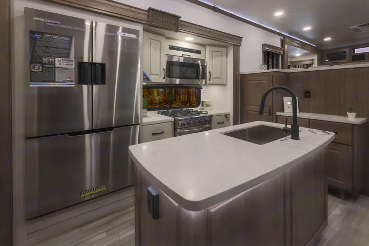 Spacious, modern RV rental kitchen featuring a large fridge, gas stove, island with sink, and sleek countertops.. Alliance RV Paradigm 2021
