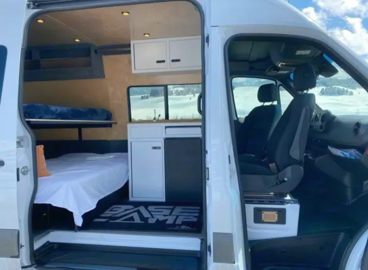 Inside this spacious RV rental camper van: multiple beds, a mini-kitchen, & driver's area. Snowy landscape visible outside.. Vanworks Base Camp 2021
