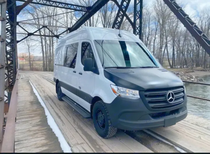 Explore with this white Mercedes-Benz Sprinter camper van, perfect for rv rental, on a scenic wooden bridge with metal trusses.. Vanworks Base Camp 2021