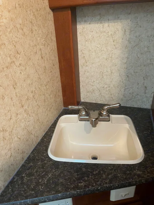 Compact RV rental bathroom featuring a white sink, chrome faucet, and dark speckled countertop.. Winnebago Other 2013
