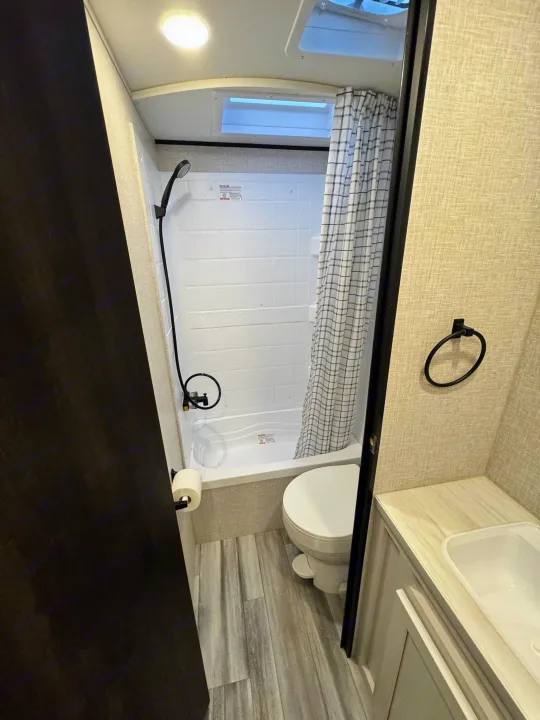Compact RV rental bathroom with a functional shower, toilet, and sink vanity, designed for efficient space use.. Jayco Jayflight 2024