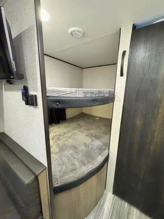 RV rental featuring cozy bunk beds, a mounted TV, and seating, perfect for mobile comfort.. Jayco Jayflight 2024