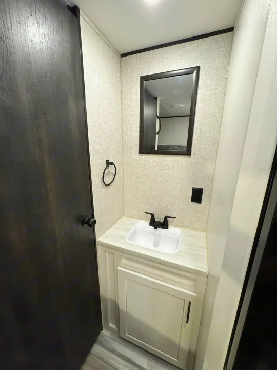Modern RV rental bathroom with a dark door, light vanity, white sink, black faucet, and framed mirror.. Jayco Jayflight 2024