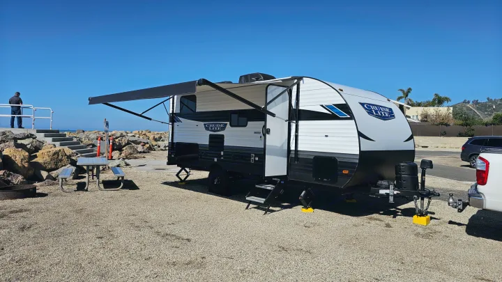 Cruise Lite RV rental at a scenic beach campsite with extended awning, ready for adventure under a clear blue sky.. Forest River Salem Cruise Lite 2024