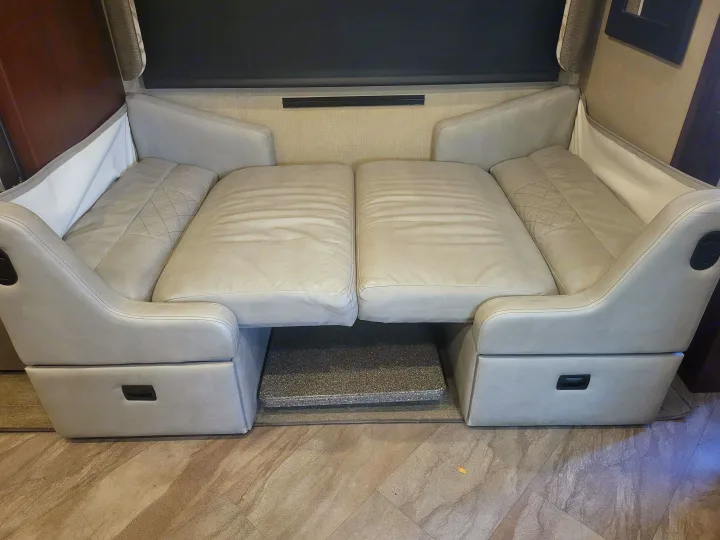 Light gray RV rental sofa, laid flat as a bed, with quilted head sections & a central step in the cozy interior.. Fleetwood Bounder 2017