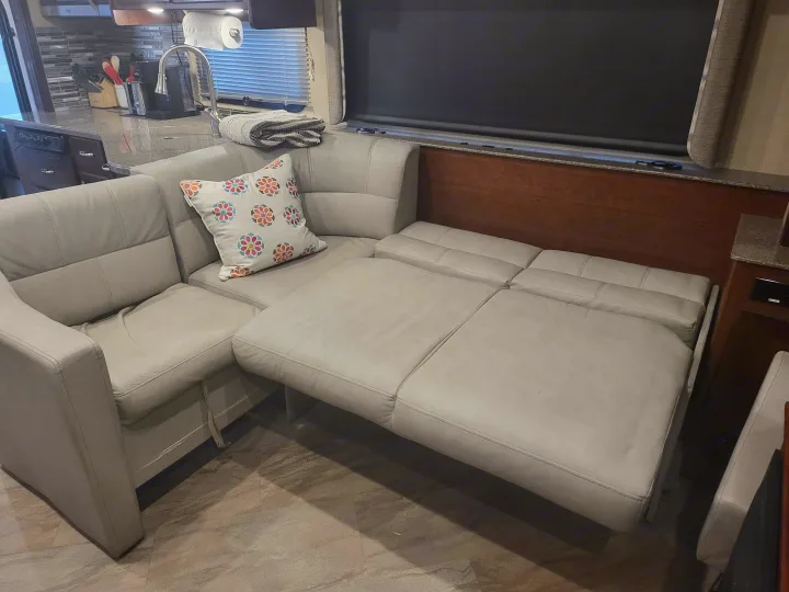 RV rental: A light gray sectional sofa converts into a bed, with a kitchen visible in the background.. Fleetwood Bounder 2017