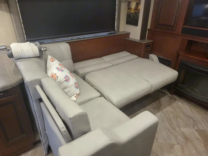 A light gray L-shaped sectional sofa, partially extended into a bed, in an RV rental living area.. Fleetwood Bounder 2017