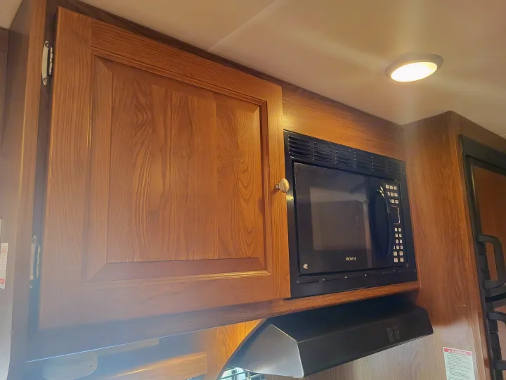 RV rental kitchen interior featuring built-in wood cabinetry, a microwave oven, and range hood for a comfortable travel experience.. Coachmen Leprechaun 2015