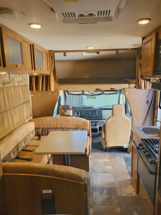 Inside a comfortable RV rental, featuring a dinette with seatbelts, a kitchen with stove/sink, front cab, and overhead bunk.. Coachmen Leprechaun 2015