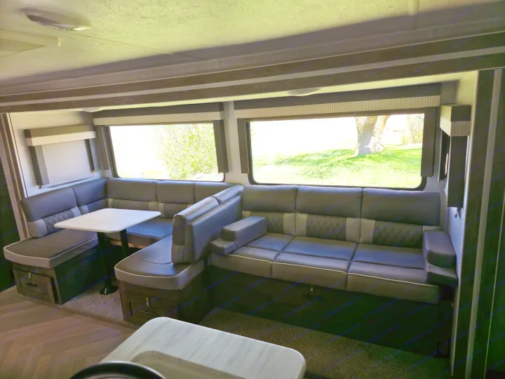 Spacious RV rental interior featuring a comfy sectional sofa and dining area with large windows showcasing bright outdoor views.. Forest River Wildwood X-Lite 2022