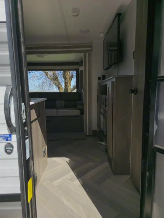 Peering into an RV rental: herringbone floor leads to a dinette and entertainment center in a spacious living area.. Forest River Wildwood X-Lite 2022