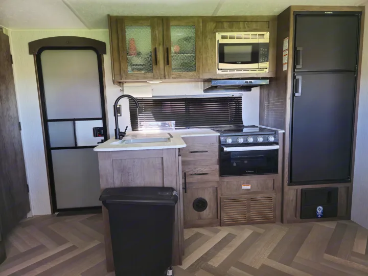 RV rental kitchen: modern interior with fridge, oven, microwave, and sink. Perfect for camping adventures.. Forest River Wildwood X-Lite 2022